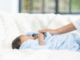 sleeping newborn in a blanked. Female who is gently caressing the baby.