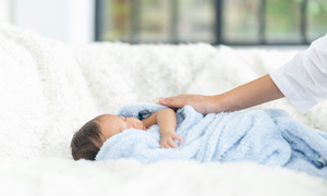 sleeping newborn in a blanked. Female who is gently caressing the baby.