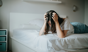 Frau auf Bett, welche sich die Haare rauft
